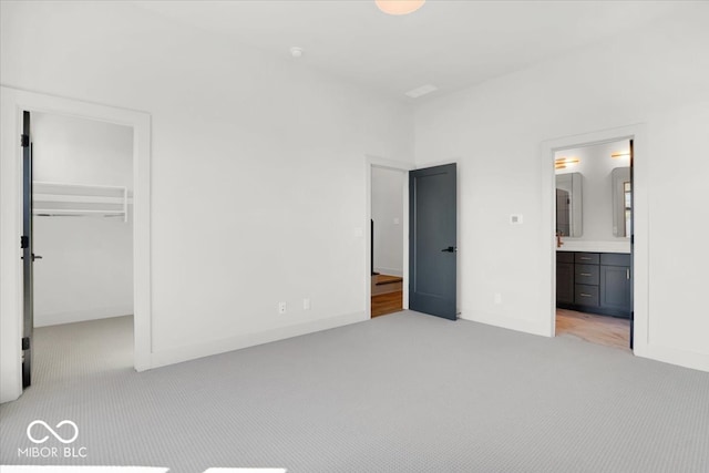 unfurnished bedroom with a closet, a spacious closet, ensuite bathroom, and light colored carpet