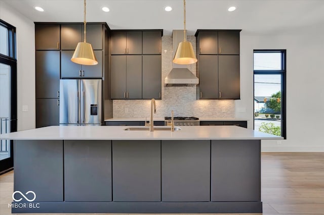 kitchen featuring light wood-type flooring, sink, decorative backsplash, stainless steel fridge with ice dispenser, and a center island with sink