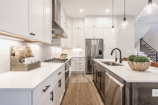 kitchen with light hardwood / wood-style floors, wall chimney exhaust hood, a kitchen island with sink, sink, and appliances with stainless steel finishes