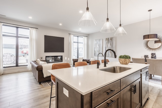 kitchen with light hardwood / wood-style floors, pendant lighting, a kitchen bar, sink, and a kitchen island with sink