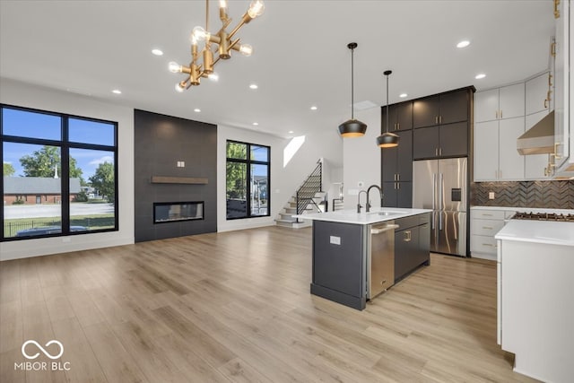 kitchen with a fireplace, pendant lighting, appliances with stainless steel finishes, light hardwood / wood-style floors, and an island with sink