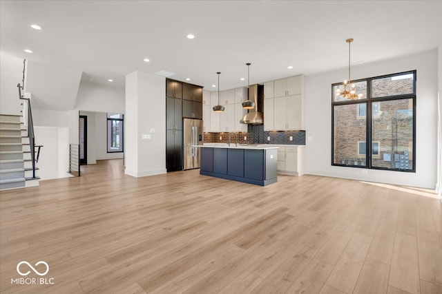 kitchen featuring wall chimney exhaust hood, stainless steel refrigerator with ice dispenser, light hardwood / wood-style floors, hanging light fixtures, and white cabinets