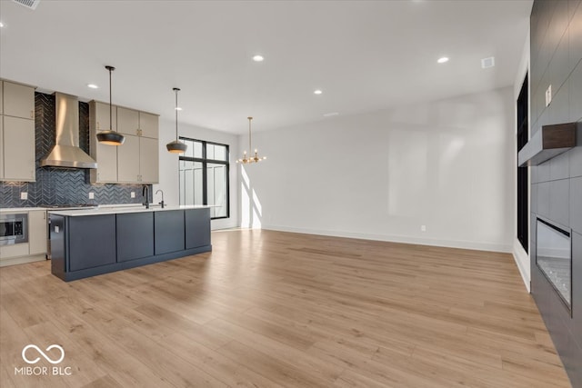 kitchen with light wood-type flooring, decorative light fixtures, wall chimney range hood, and a chandelier