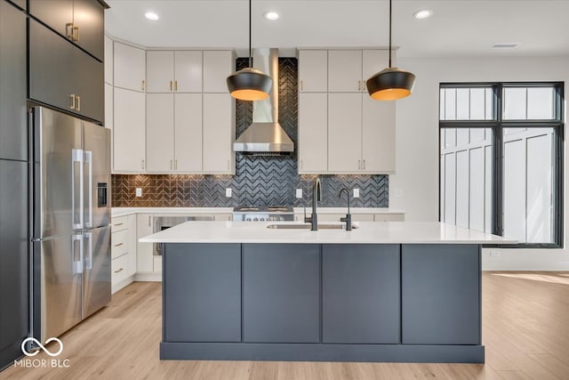 kitchen with light wood-type flooring, sink, an island with sink, high quality fridge, and wall chimney range hood