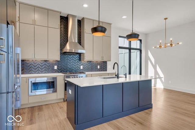 kitchen with light hardwood / wood-style flooring, stainless steel appliances, sink, wall chimney range hood, and a kitchen island with sink