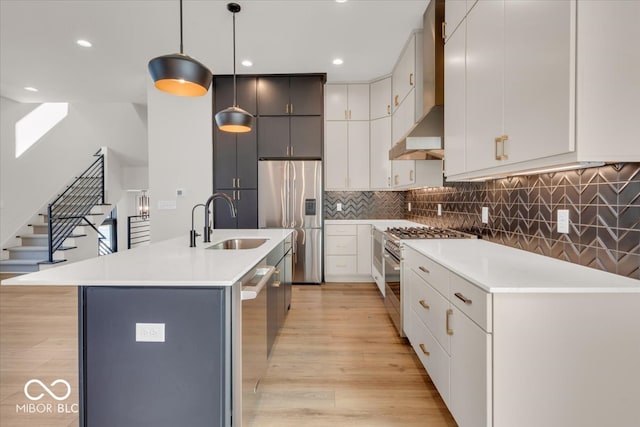 kitchen with light wood-type flooring, stainless steel appliances, decorative light fixtures, sink, and a center island with sink