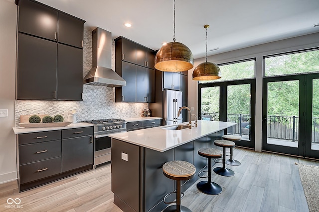 kitchen featuring light countertops, hanging light fixtures, appliances with stainless steel finishes, a sink, and wall chimney exhaust hood