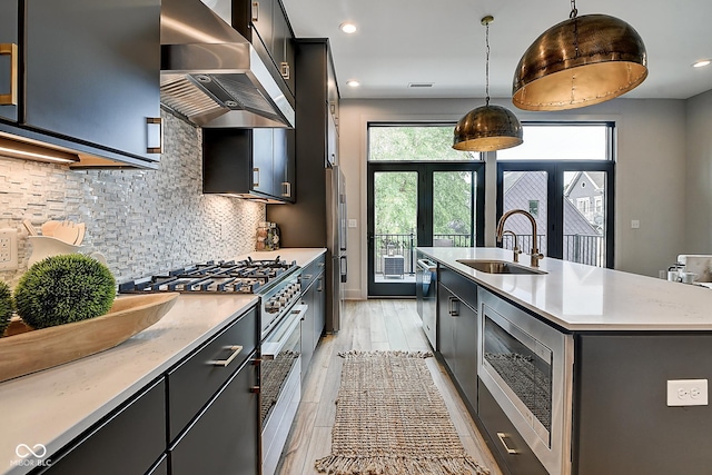 kitchen with stainless steel appliances, a sink, light countertops, range hood, and pendant lighting