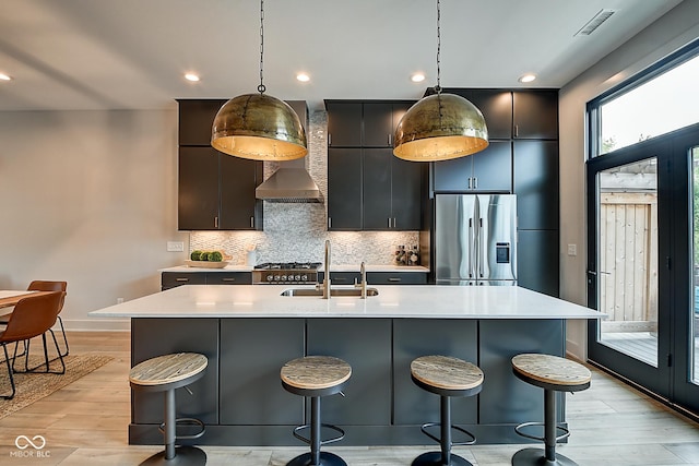 kitchen with a kitchen island with sink, appliances with stainless steel finishes, light countertops, and pendant lighting