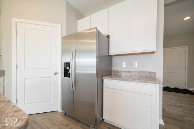 kitchen with light stone countertops, stainless steel fridge, hardwood / wood-style flooring, and white cabinetry