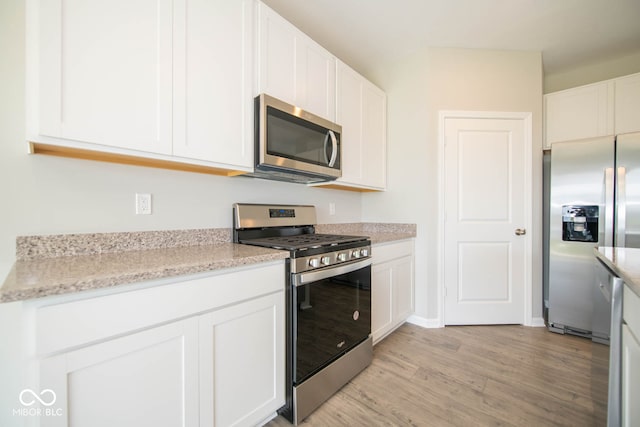 kitchen featuring appliances with stainless steel finishes, white cabinets, light stone countertops, and light hardwood / wood-style flooring