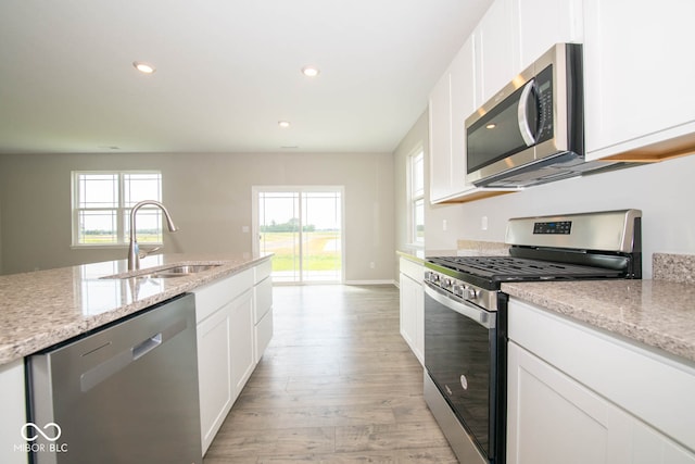 kitchen featuring white cabinetry, light stone countertops, light wood-type flooring, stainless steel appliances, and sink