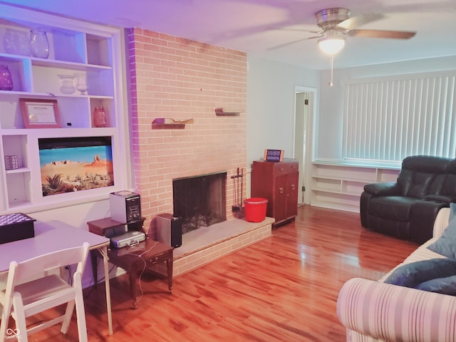 living room featuring built in shelves, hardwood / wood-style flooring, a brick fireplace, and ceiling fan