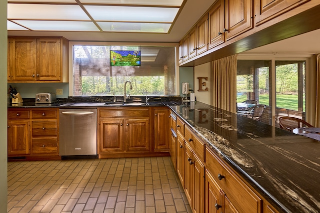 kitchen with stainless steel dishwasher, sink, plenty of natural light, and dark stone countertops