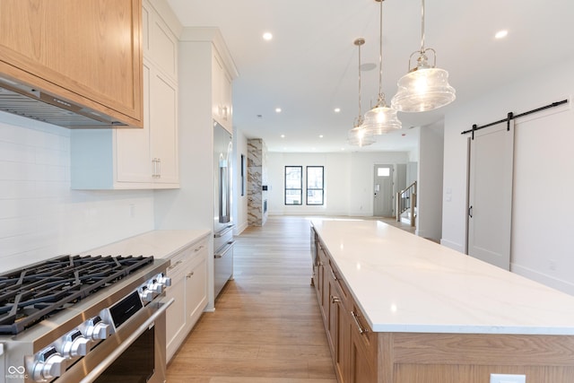 kitchen with a barn door, appliances with stainless steel finishes, a spacious island, decorative light fixtures, and white cabinets