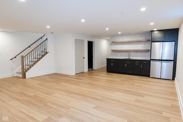 kitchen with light wood-type flooring, sink, backsplash, and stainless steel refrigerator