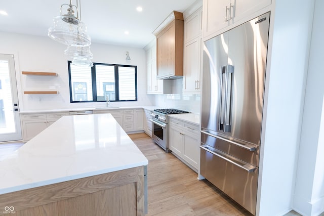 kitchen featuring light stone countertops, premium appliances, white cabinetry, backsplash, and hanging light fixtures