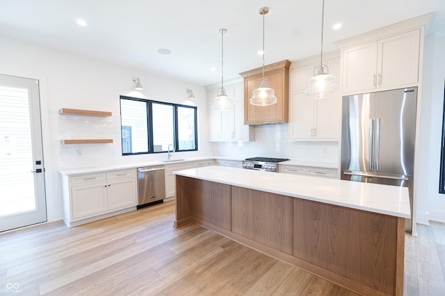 kitchen featuring pendant lighting, a kitchen island, stainless steel appliances, sink, and light hardwood / wood-style flooring