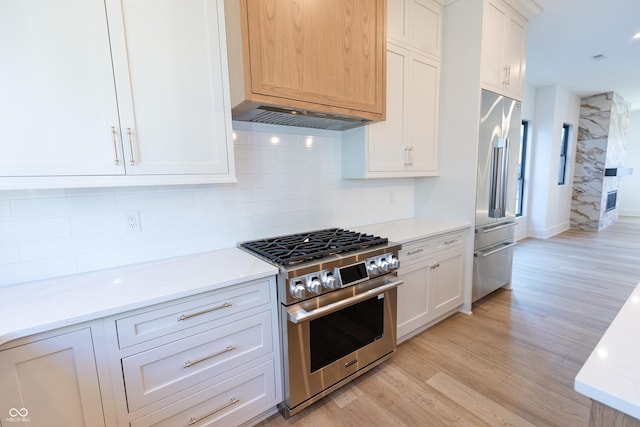 kitchen featuring high end appliances, light hardwood / wood-style floors, white cabinets, and light stone counters