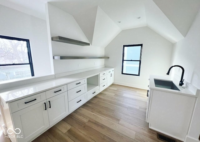 interior space featuring lofted ceiling, light wood-type flooring, sink, and white cabinetry