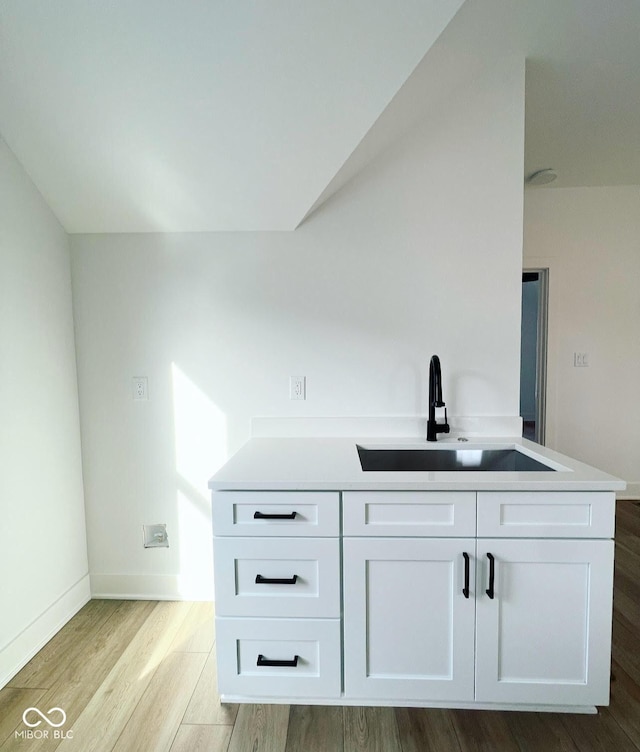 bar with light wood-type flooring, sink, and white cabinetry