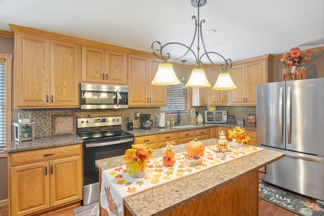 kitchen featuring appliances with stainless steel finishes, a kitchen island, backsplash, decorative light fixtures, and light hardwood / wood-style flooring