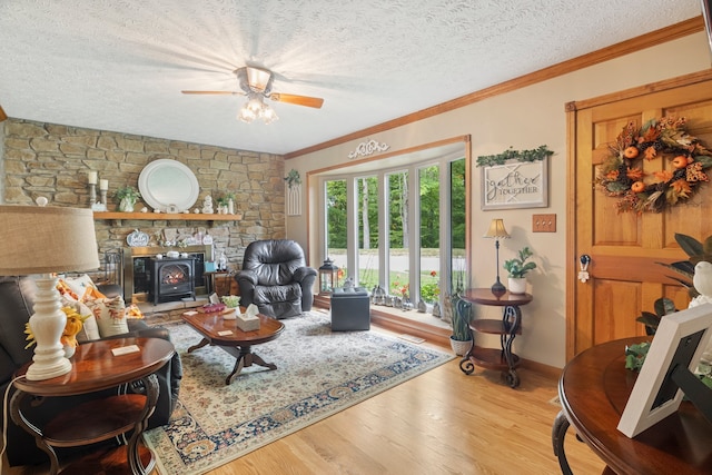 living room featuring a textured ceiling, ceiling fan, a stone fireplace, and light hardwood / wood-style flooring