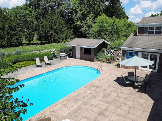 view of pool with a grill, an outbuilding, and a patio area