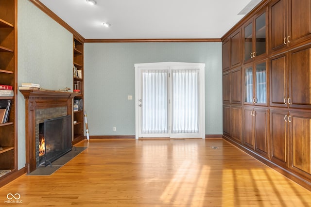 unfurnished living room featuring built in shelves, crown molding, and light wood-type flooring