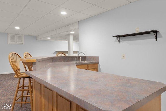 kitchen with a paneled ceiling, sink, carpet flooring, a kitchen bar, and kitchen peninsula