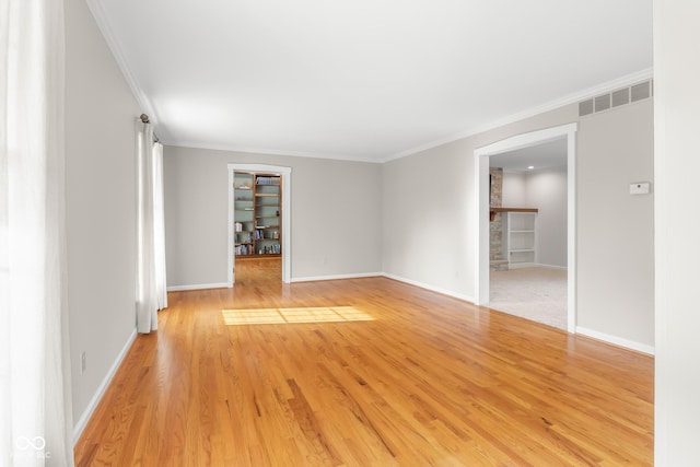 unfurnished room featuring crown molding, light wood-type flooring, and built in shelves