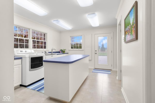 kitchen featuring light tile patterned flooring, a kitchen island, white cabinets, ornamental molding, and washing machine and dryer