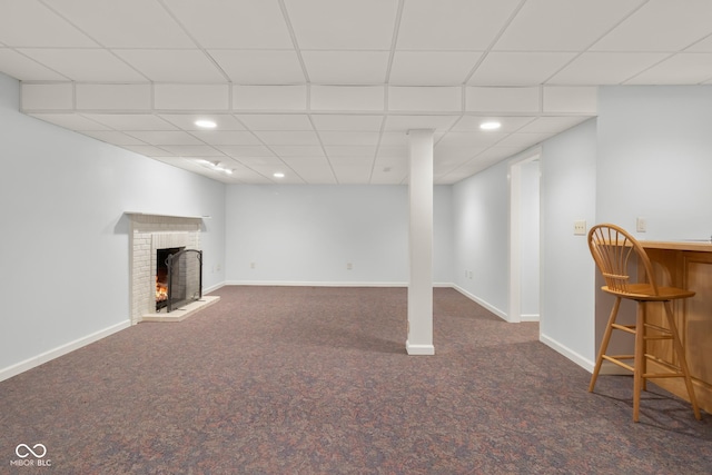 basement featuring a brick fireplace, dark carpet, a paneled ceiling, and bar area