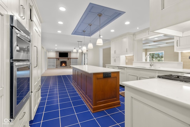 kitchen with sink, white cabinetry, a center island, a large fireplace, and pendant lighting