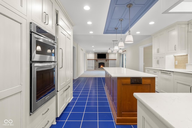 kitchen featuring dishwasher, white cabinets, a center island, a brick fireplace, and stainless steel double oven