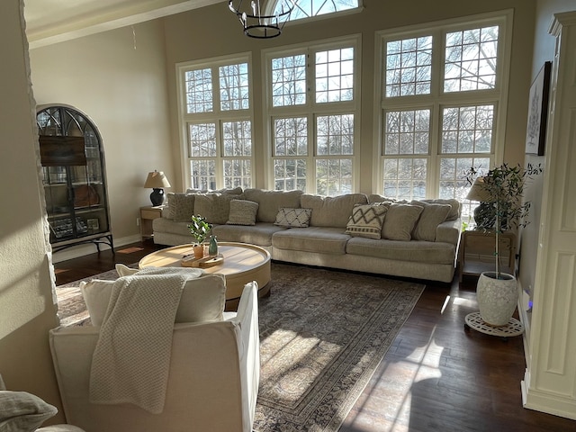 living room featuring a healthy amount of sunlight, a towering ceiling, a chandelier, and dark wood-type flooring