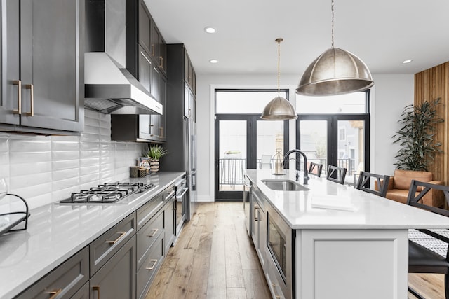 kitchen featuring wall chimney range hood, a kitchen island with sink, a breakfast bar area, sink, and tasteful backsplash