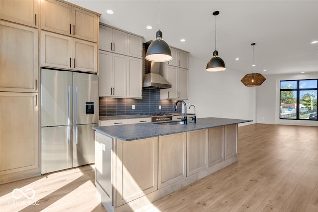 kitchen featuring light wood-type flooring, stainless steel appliances, an island with sink, sink, and wall chimney exhaust hood