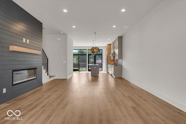 unfurnished living room with a large fireplace, baseboards, stairs, light wood-type flooring, and recessed lighting