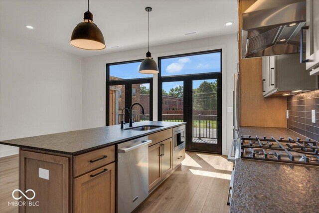 kitchen featuring appliances with stainless steel finishes, light hardwood / wood-style floors, an island with sink, sink, and wall chimney range hood