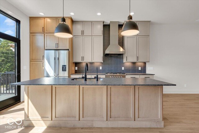 kitchen with stainless steel fridge, wall chimney range hood, and a kitchen island with sink