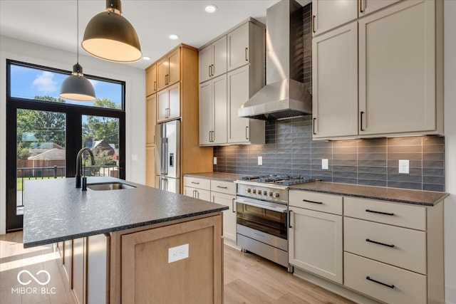 kitchen with light wood-type flooring, stainless steel appliances, sink, a center island with sink, and wall chimney range hood