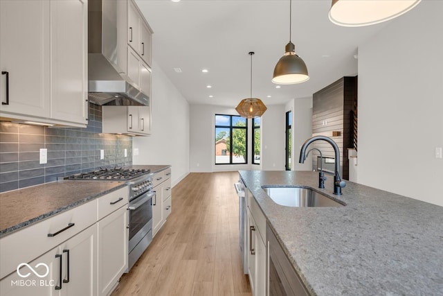 kitchen featuring light wood-type flooring, decorative light fixtures, stainless steel appliances, sink, and wall chimney range hood