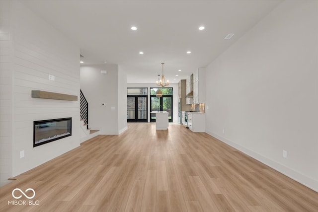 unfurnished living room with light wood-type flooring, a fireplace, and a chandelier