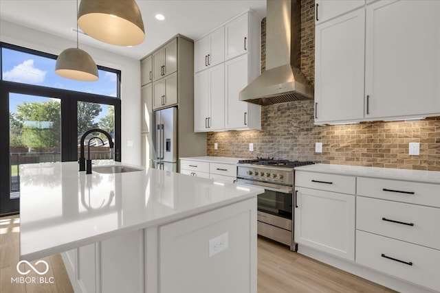 kitchen with hanging light fixtures, high end appliances, sink, wall chimney exhaust hood, and a kitchen island with sink