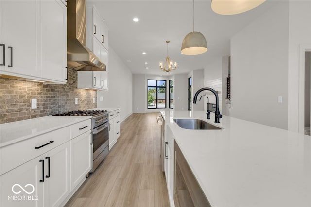 kitchen featuring decorative light fixtures, wall chimney exhaust hood, light hardwood / wood-style flooring, high end stove, and sink