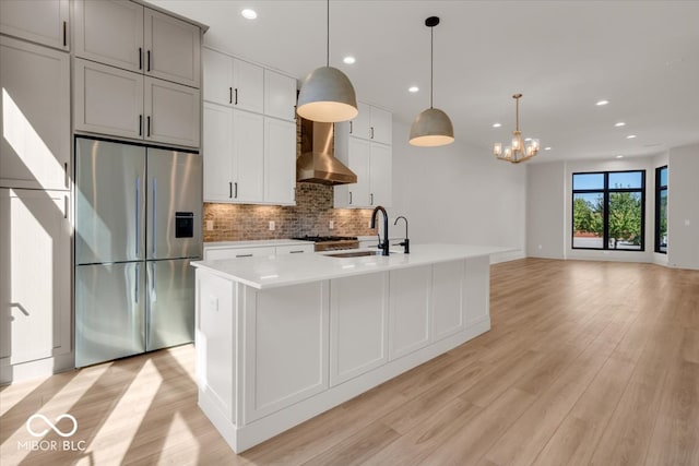 kitchen featuring wall chimney exhaust hood, light hardwood / wood-style floors, stainless steel fridge with ice dispenser, and an island with sink