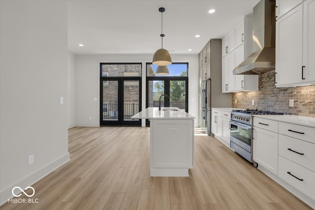 kitchen with high end appliances, a kitchen island with sink, sink, wall chimney range hood, and light wood-type flooring