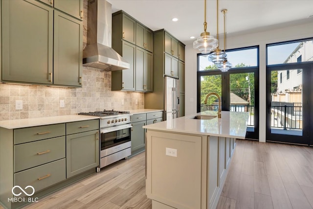 kitchen with high end stainless steel range, light wood-type flooring, sink, wall chimney exhaust hood, and a center island with sink