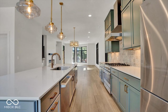 kitchen featuring light wood-type flooring, appliances with stainless steel finishes, sink, wall chimney range hood, and a center island with sink